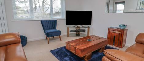 A living room with a TV, a blue chair, a wooden coffee table, and leather sofas.
