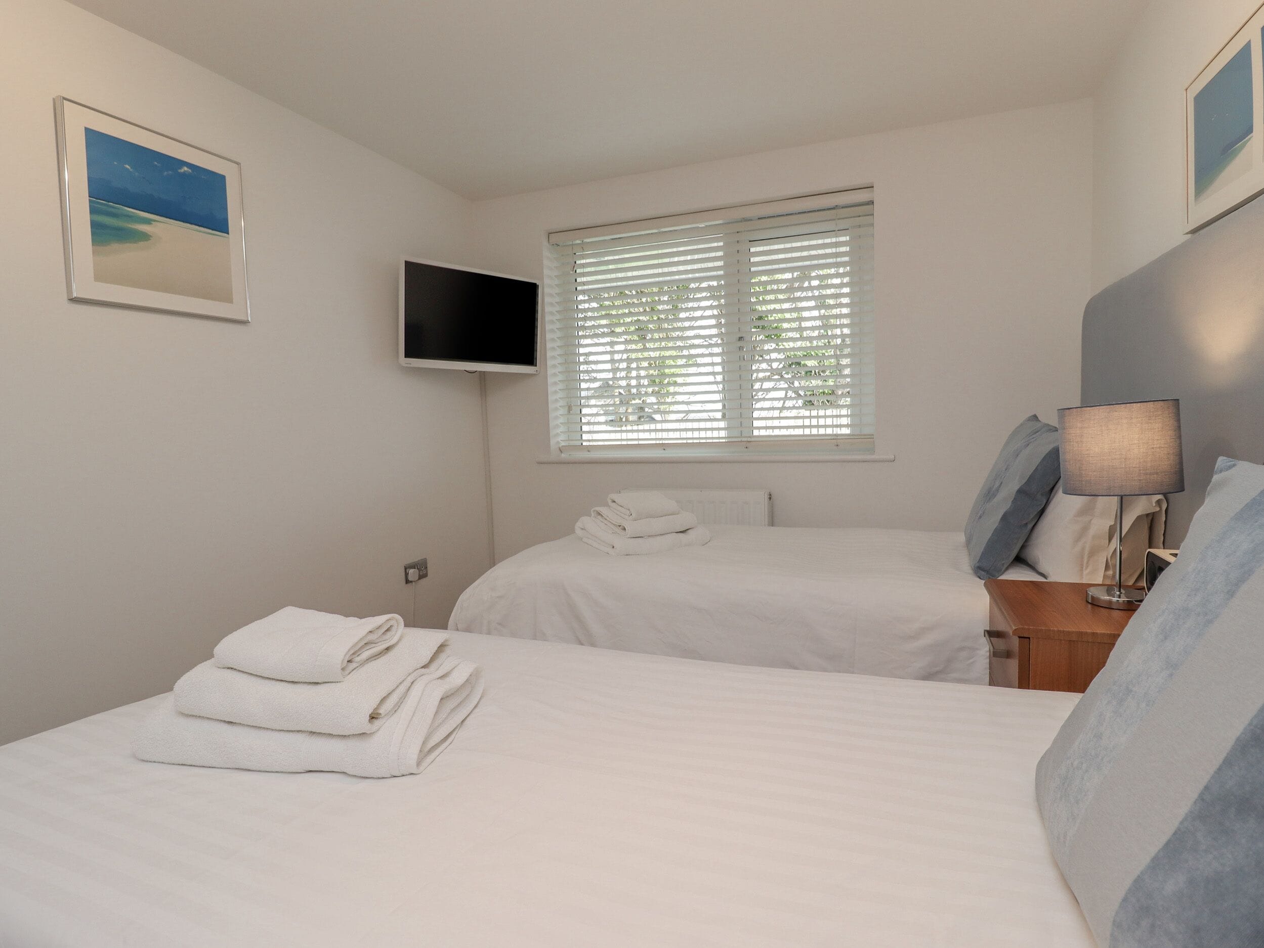 A bedroom with two beds, a TV, and a window with blinds.