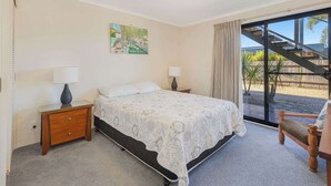 A bedroom with a bed, two bedside tables with lamps, a painting on the wall, and a view of a staircase and outdoor area.