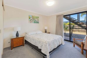 A bedroom with a bed, two bedside tables with lamps, a painting on the wall, and a view of a staircase and outdoor area. - Golden Sands (Meribula)