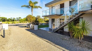 A modern building with a balcony, a staircase, and a gravel driveway.