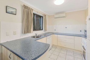 A kitchen with a granite countertop, a window with curtains, a sink, and an air conditioning unit.