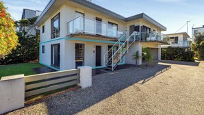 A modern two-story house with a balcony, a staircase, and a gravel driveway.
