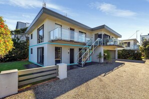 A modern two-story house with a balcony, a staircase, and a gravel driveway.