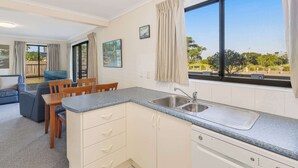 A compact kitchen with a sink, a dining area with a table and chairs, and a large window with curtains.