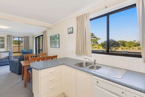 A compact kitchen with a sink, a dining area with a table and chairs, and a large window with curtains.