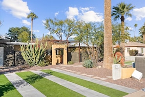 A residential property with a well-maintained lawn, a variety of cacti and palm trees, and a clear sky.