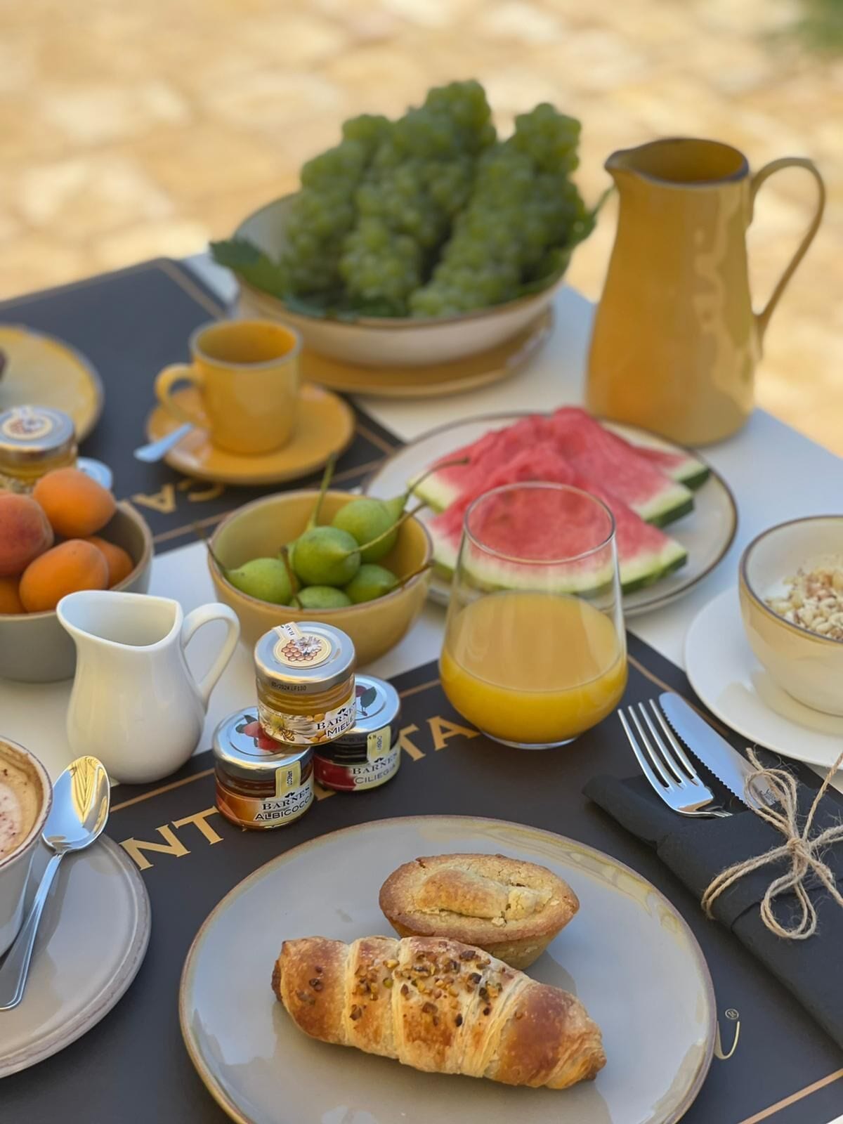 A breakfast table with croissants, fruit, and a jug of orange juice.