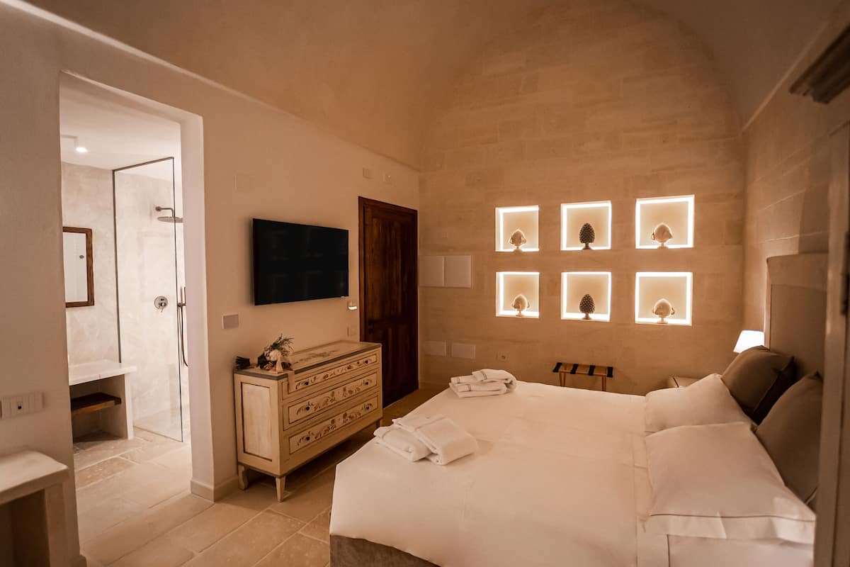 Un dormitorio con una cama grande, un aparador de madera, un televisor montado en la pared y varios apliques de luz.