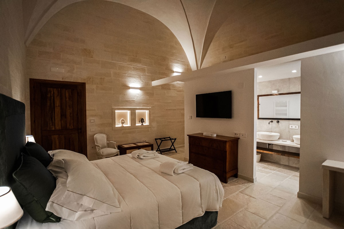 Un dormitorio moderno con una cama grande, una puerta de madera, una silla, un escritorio y un televisor de pantalla plana montado en la pared.
