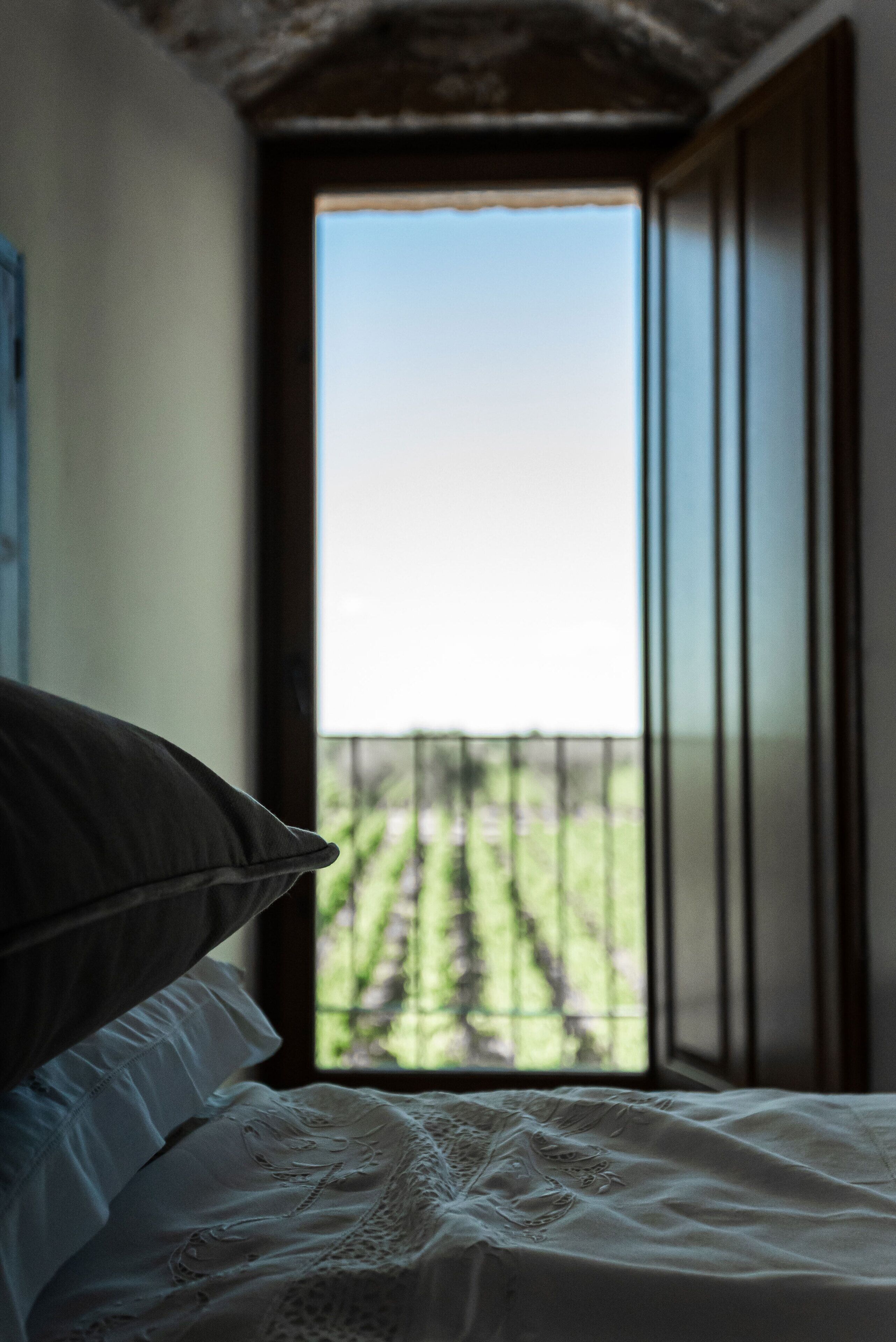 A bedroom with a bed, a window, and a view of a balcony with greenery.