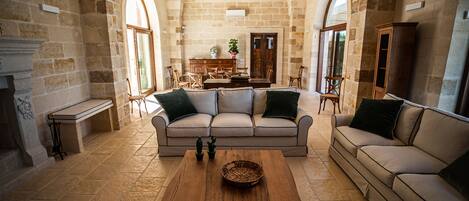 Un salón amplio con pared de piedra, una mesa de centro de madera, un sofá color beige y una zona de comedor con mesa y sillas de madera.