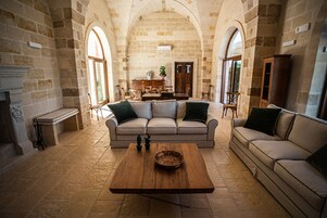 Un salón amplio con pared de piedra, una mesa de centro de madera, un sofá color beige y una zona de comedor con mesa y sillas de madera.