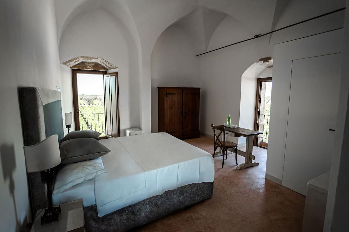 Un dormitorio con cama, escritorio y silla. Se ve una ventana con vistas al exterior.