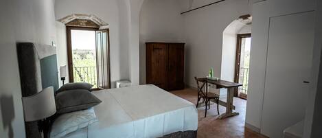 Un dormitorio con cama, escritorio y silla. Se ve una ventana con vistas al exterior.