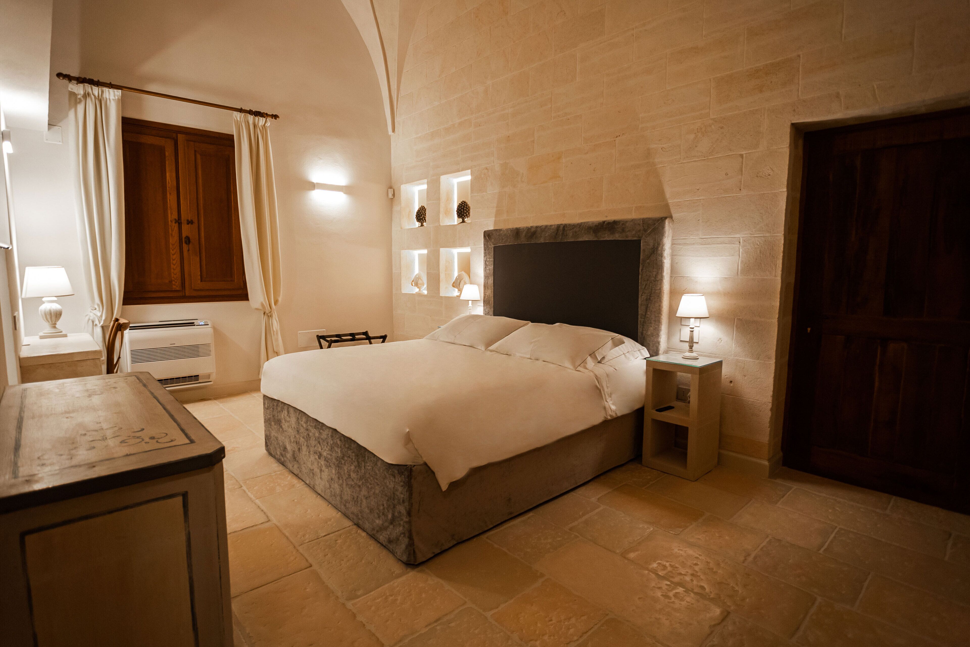 Une chambre à coucher avec un lit, des tables de chevet, une armoire en bois et un mur en pierre.