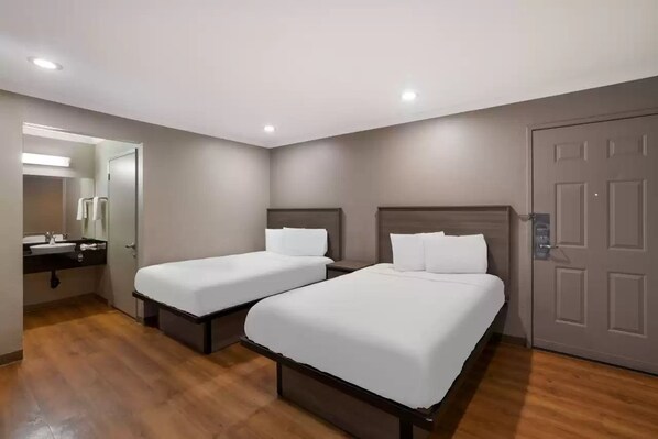 Una habitación de hotel con dos camas individuales, un baño con lavamanos y espejo, y una puerta.