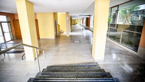 Un pasillo interior espacioso con suelo de mármol, paredes amarillas y grandes ventanales que dan a vistas de vegetación.
