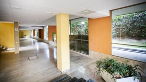 Un pasillo amplio con ventanas grandes, una pared amarilla y una planta en primer plano.
