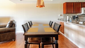 A dining area with a wooden table and chairs, a hanging pendant light, and a kitchen with wooden cabinets and a microwave. - Condo with Golf Course & Camelback Mountain Views. (Scottsdale)