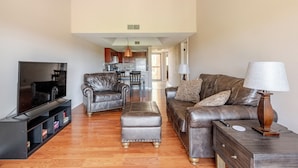 A living room with a flat-screen TV, leather sofas, ottoman, and a wooden side table with a lamp. - Condo with Golf Course & Camelback Mountain Views. (Scottsdale)
