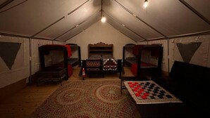 A tented room with bunk beds, a central bed, a chess table, and a patterned rug. - Maples Farm Fresh Eggs (Nashville)