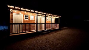 A wooden cabin with multiple windows and a balcony, illuminated at night. - Maples Farm Fresh Eggs (Nashville)