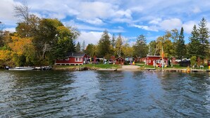 A lakeside property with multiple red houses, docked boats, and a grassy area with colorful chairs. - River View 2 Bedroom Cottage 11 (Hastings)