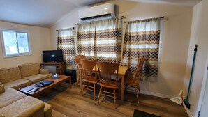 A living room with a sofa, TV, wooden table, and chairs. - River View 2 Bedroom Cottage 11 (Hastings)