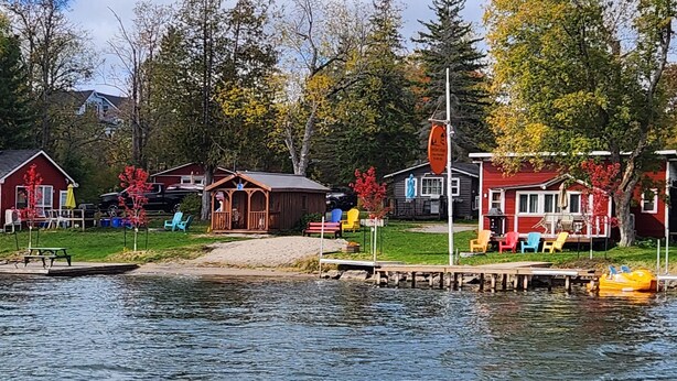 A lakeside cabin area with docked boats, a picnic table, and a small dock. - River View 2 Bedroom Cottage 11 (Hastings)