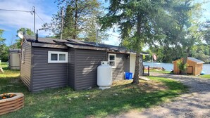 A small cabin with a propane tank, a satellite dish, and a dock by a lake. - River View 2 Bedroom Cottage 11 (Hastings)