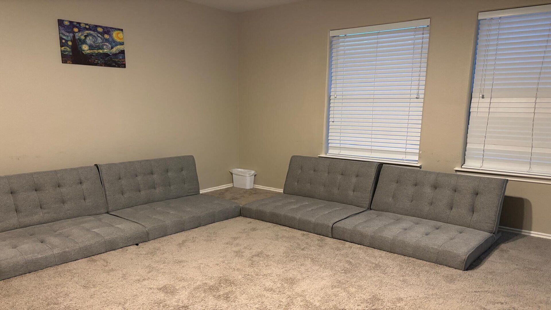 A living room with a grey sectional sofa, beige carpet, and a painting on the wall.