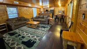 A cozy cabin interior with wooden walls, a living area with sofas and a coffee table, a kitchen with wooden cabinets, and a dining area with a table and chairs. - Secluded 1 bd 2 bath cabin with Great View (Sevier County)