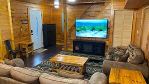 A cozy living room with a wooden interior, a flat-screen TV mounted on the wall, a sofa, a coffee table, and a staircase leading upstairs. - Secluded 1 bd 2 bath cabin with Great View (Sevier County)