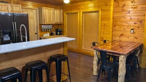 A wooden cabin interior with a kitchen area, bar stools, a wooden dining table, and a refrigerator. - Secluded 1 bd 2 bath cabin with Great View (Sevier County)