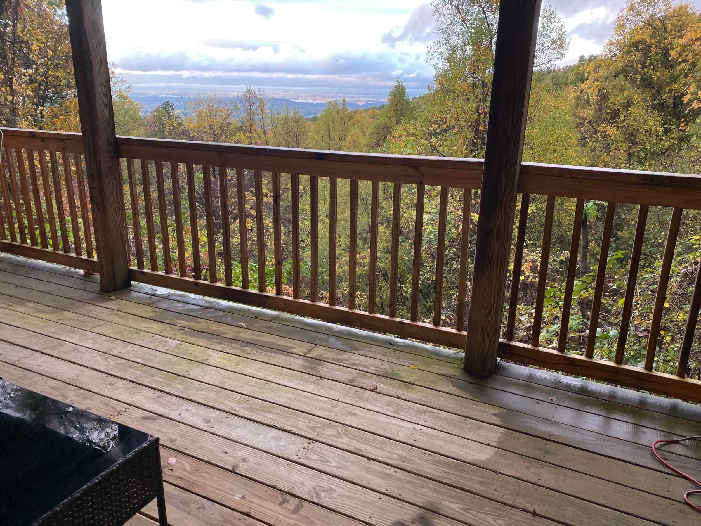 Une terrasse en bois dotée d’une rambarde, qui offre une vue sur une zone boisée et un paysage lointain.