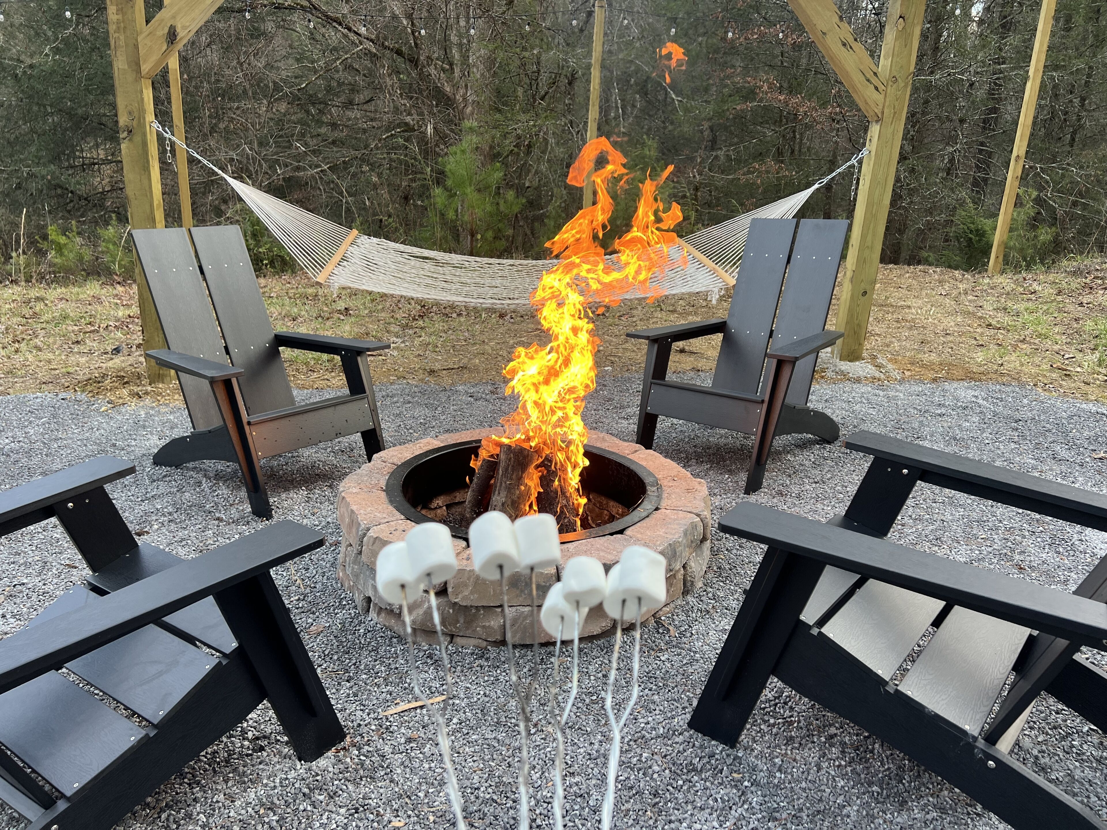 A fire pit with logs and a hammock between two chairs.