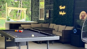 A pool table with balls, a neon sign reading "The Out Door," and a hammock in a room with a green wall and wooden ceiling. - Flat Fenced yard, hot tub , wifi, pool table (Sevier County)