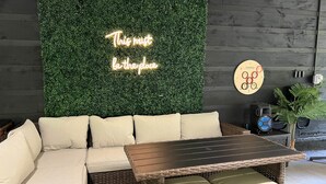 A modern lounge area with a sectional sofa, a wooden coffee table, a green wall with a neon sign, a wall clock, and a speaker. - Flat Fenced yard, hot tub , wifi, pool table (Sevier County)