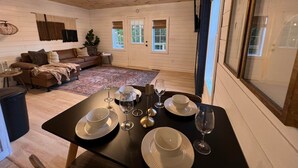 A cozy living room with a wooden ceiling, a dining table set with plates and glasses, a sofa with cushions, and a large window with blinds. - Flat Fenced yard, hot tub , wifi, pool table (Sevier County)