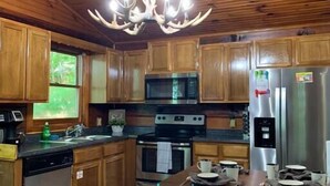 A wooden-paneled kitchen with a central island, stainless steel appliances, and a unique antler chandelier. - Log Cabin Minutes to Dollywood all Pigeon Forge (Sevier County)