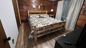 A wooden-paneled bedroom with a bed, a lamp, and a TV stand. - Log Cabin Minutes to Dollywood all Pigeon Forge (Sevier County)