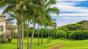 Un terrain de golf avec une maison en arrière-plan, entouré de palmiers et d’une végétation luxuriante.