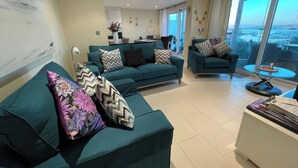 A modern living room with teal sofas, patterned cushions, and a glass table. - Bear's Apartment (Portland)