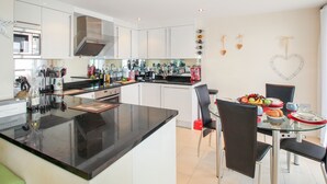 A modern kitchen with white cabinets, a black countertop, and a glass dining table with chairs. - Bear's Apartment (Portland)