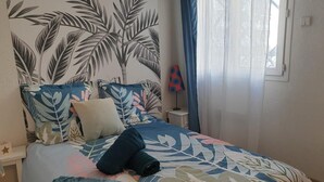 Ett sovrum med en säng, ett nattduksbord, en lampa och ett fönster med gardiner.