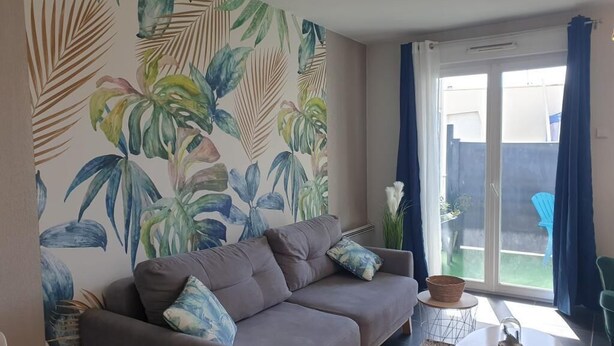 Ett vardagsrum med en grå soffa, ett litet runt bord och ett stort fönster med blå gardiner.