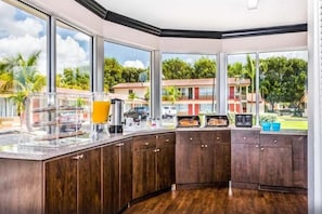 A kitchen with a large window, wooden cabinets, and a breakfast bar with various items. - Econo Lodge Inn & Suites Florida City (Florida City)
