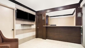 Un intérieur moderne avec un téléviseur à écran plat fixé au mur, un banc en bois foncé et un fauteuil en osier.