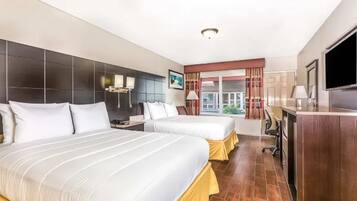 Quarto de hotel com duas camas, uma escrivaninha, uma televisão e uma janela com cortinas.